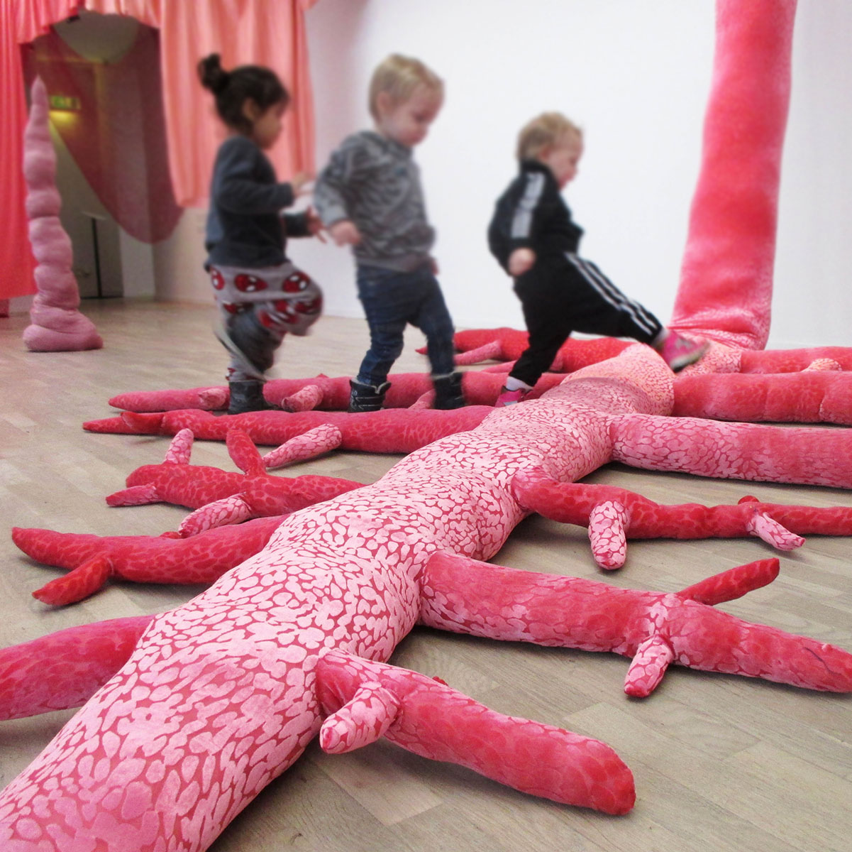 Tre barn går över en rosa textilskulptur.