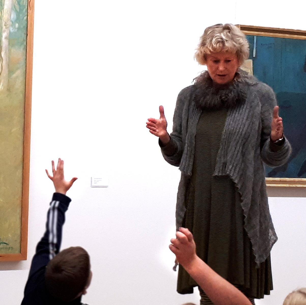 En kvinna med blont hår visar konst för barn som räcker upp handen.
