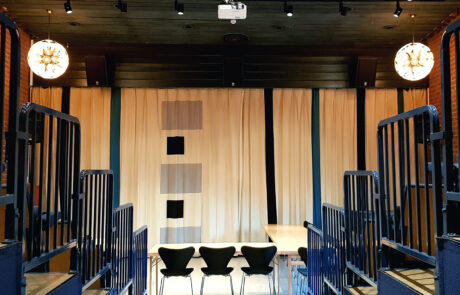 Hörsalen Harlekinen med tre svarta stolar uppställda på rad. I bakgrunden syns ett draperi i vitt, svart och grått.