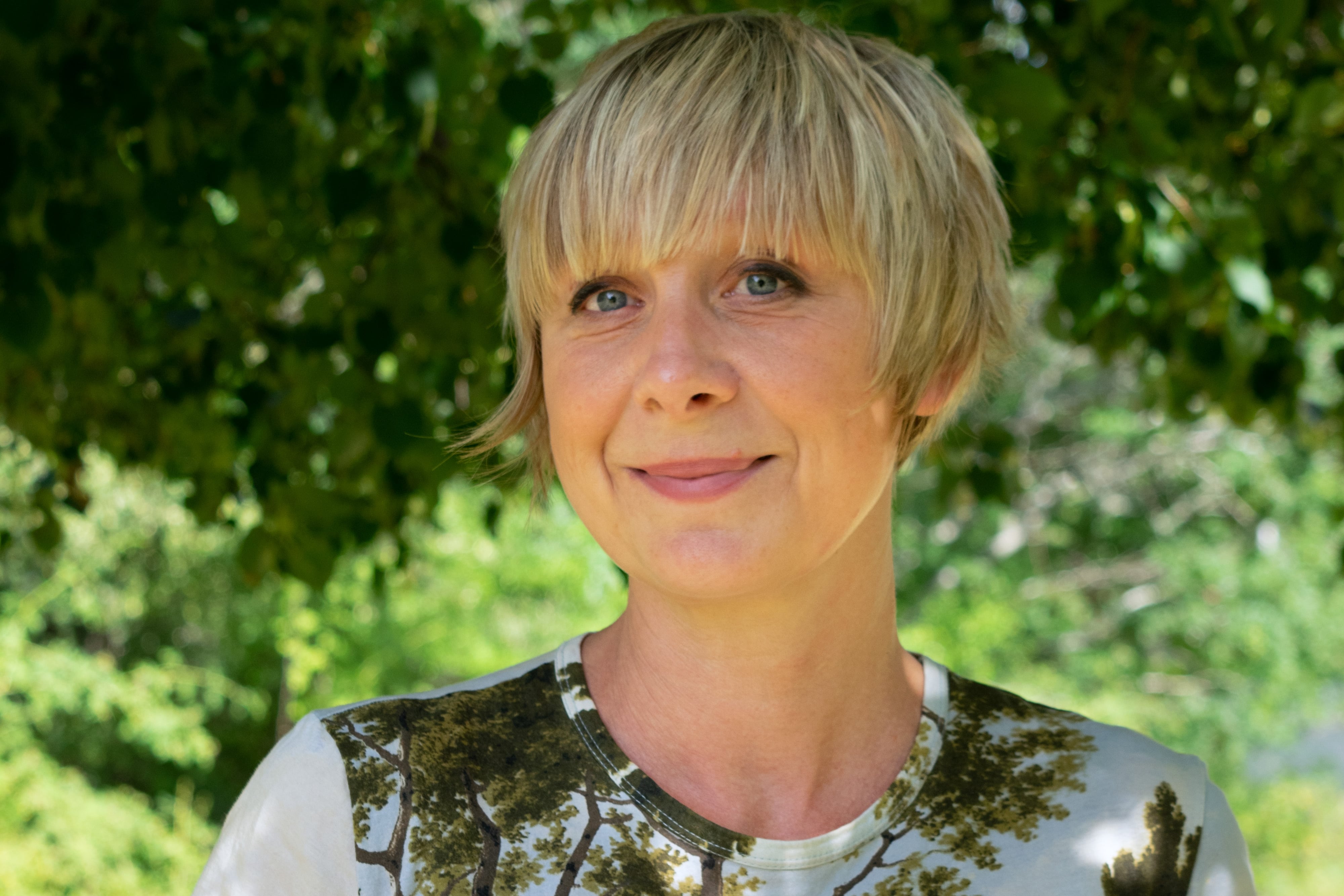 Porträttbild av illustratören Lena Sjöberg under ett träd.