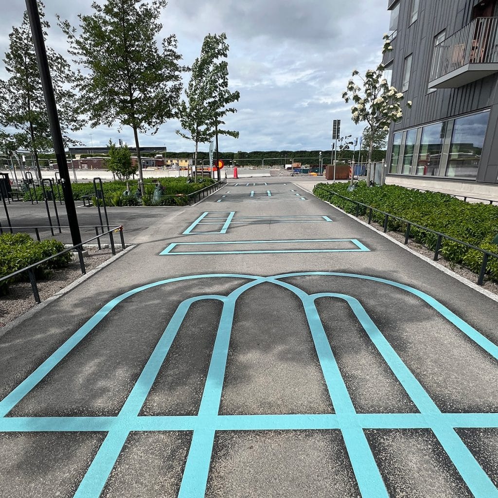 Srora bokstäver tryckta på asfalten, blå kontur mot grå asfalt