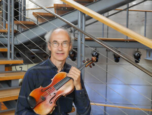 Porträtt av violinisten Matts Eriksson sittandes i trappa hållandes fiol. 